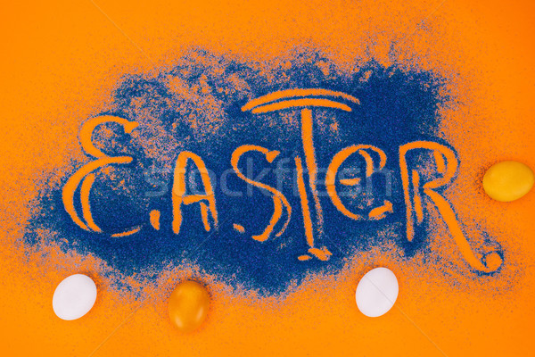 top view of easter sign made of blue sand with chicken eggs on orange Stock photo © LightFieldStudios