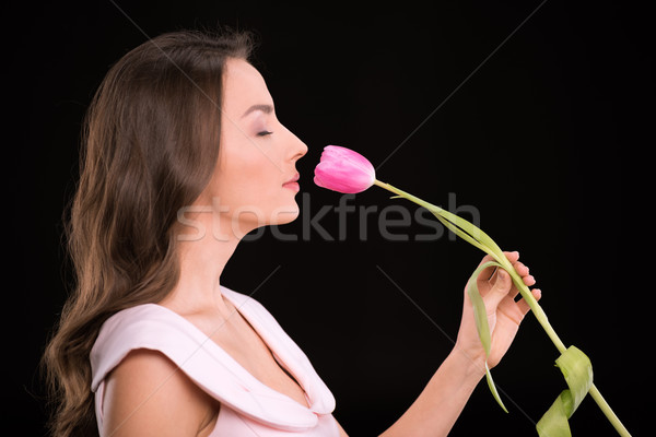 Side view of beautiful young woman with closed eyes smelling tulip flower on black, international wo Stock photo © LightFieldStudios