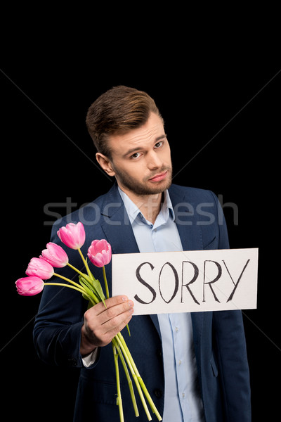 Upset young man holding pink tulips and sorry sign on black  Stock photo © LightFieldStudios