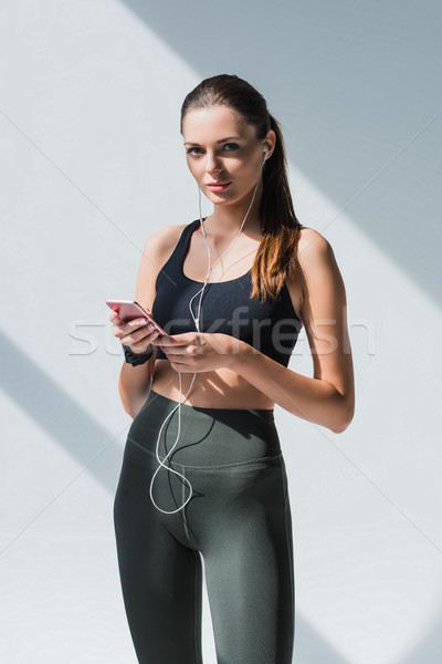 Stock photo: sportswoman in earphones using smartphone