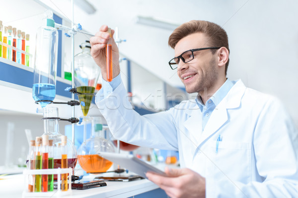 Young smiling man scientist holding digital tablet and looking at test tube in lab Stock photo © LightFieldStudios