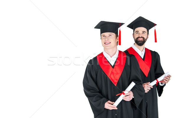 Two young men in academic caps holding diplomas and smiling on white Stock photo © LightFieldStudios