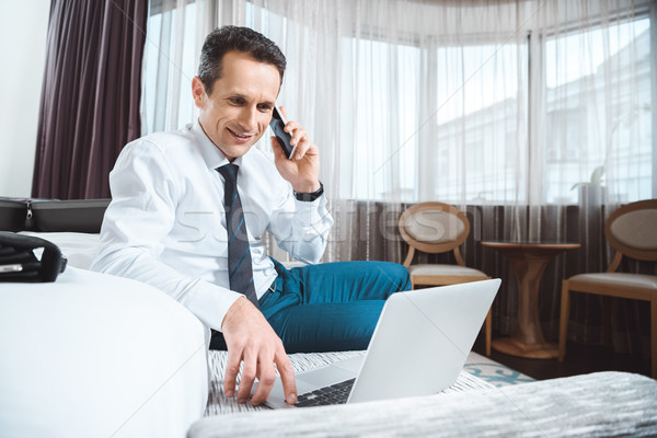 Stockfoto: Zakenman · telefoon · met · behulp · van · laptop · glimlachend · praten · hotelkamer