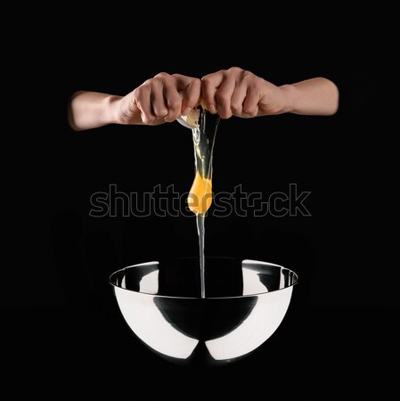cropped image of woman holding broken chicken egg above bowl isolated on black Stock photo © LightFieldStudios