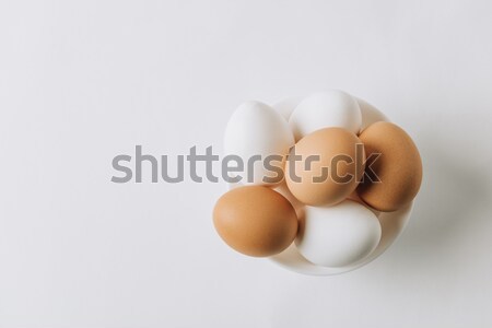 top view of white and brown eggs laying on white plate on white background Stock photo © LightFieldStudios