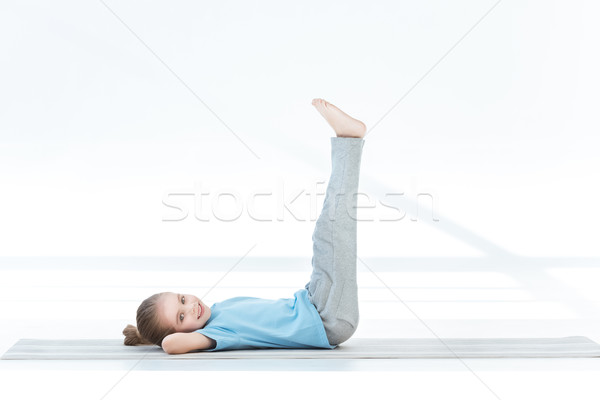Cute little girl exercising on yoga mat and smiling at camera Stock photo © LightFieldStudios