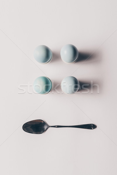 top view of four easter eggs on stands and spoon on white surface Stock photo © LightFieldStudios
