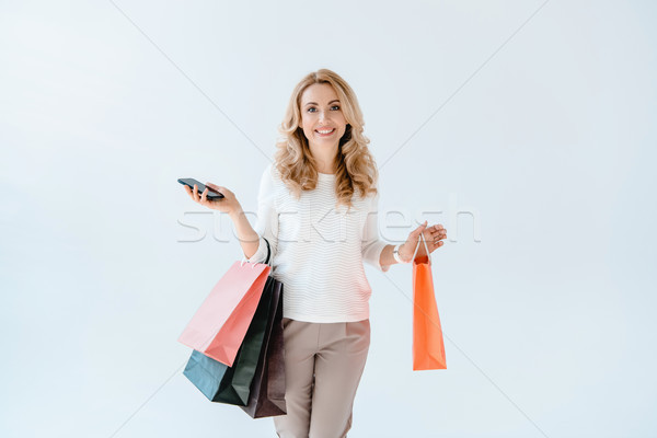 Gyönyörű mosolygó nő tart okostelefon bevásárlótáskák szürke Stock fotó © LightFieldStudios