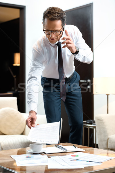Businessman reading paperwork and talking on phone Stock photo © LightFieldStudios
