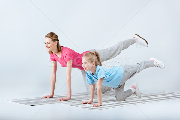 smiling sporty mother and daughter exercising on mats together on white Stock photo © LightFieldStudios