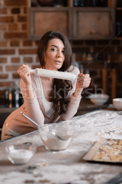 'Attractive young woman with rolling pin leaning at kitchen table and looking at camera Stock photo © LightFieldStudios