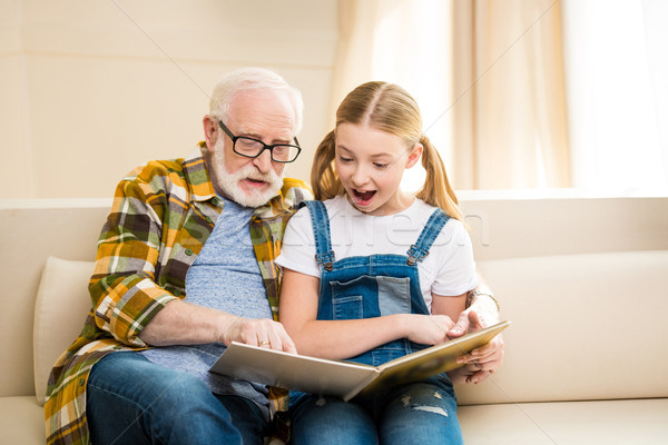 Happy grandfather and granddaughter reading book together at home Stock photo © LightFieldStudios