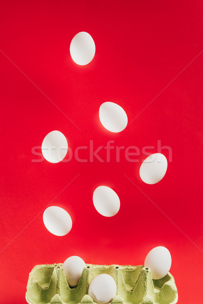close up view of levitating raw chicken eggs and cardboard egg box isolated on red Stock photo © LightFieldStudios