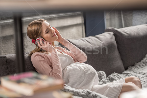 Kobieta w ciąży słuchawki młodych posiedzenia sofa słuchanie muzyki Zdjęcia stock © LightFieldStudios