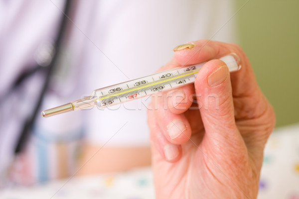 An old woman holding a clinical thermometer in herhand, a blurred image of a doctor with stethoscope Stock photo © Lighthunter
