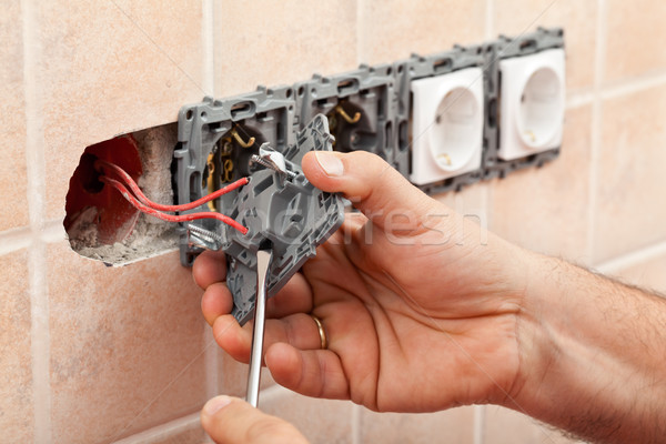 Electrician hands tighten electrical wires in wall fixture or so Stock photo © lightkeeper