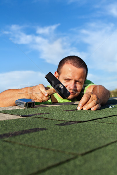 Man fastening bitumen roof shingles with nails and hammer Stock photo © lightkeeper