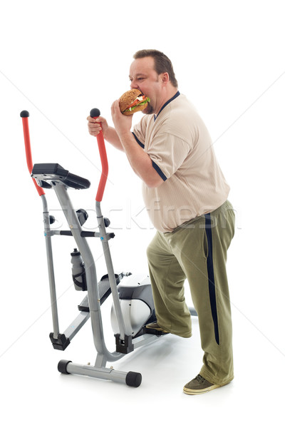 Overweight man eating by an exercising device Stock photo © lightkeeper
