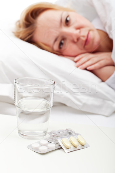 Woman laying sick with pills and glass of water Stock photo © lightkeeper