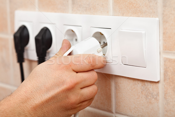 Hand plugging a power cord into electrical wall fixture Stock photo © lightkeeper