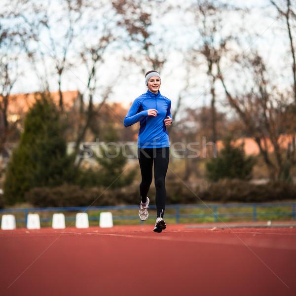 Stock photo: Young woman running at a track and field stadium