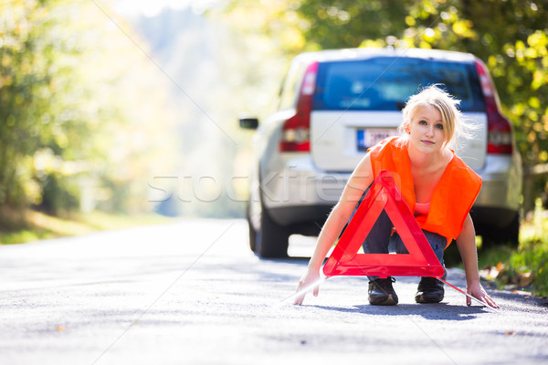 Stock photo: Young female driver wearing a high visibility vest, setting up t
