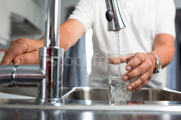 Hands of a senior man pouring a glass of water in a modern kitchen Stock photo © lightpoet