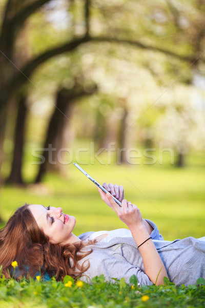 Stock photo: Young woman using her tablet computer while relaxing outdoors 