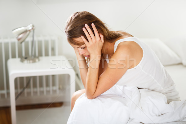 Stock photo: Pretty, young woman sitting on bed looking unhappy, depressed