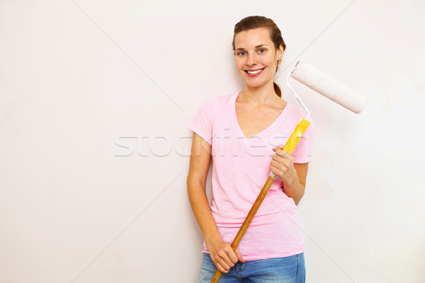Stock photo: Happy woman with roller brush standing against wall.