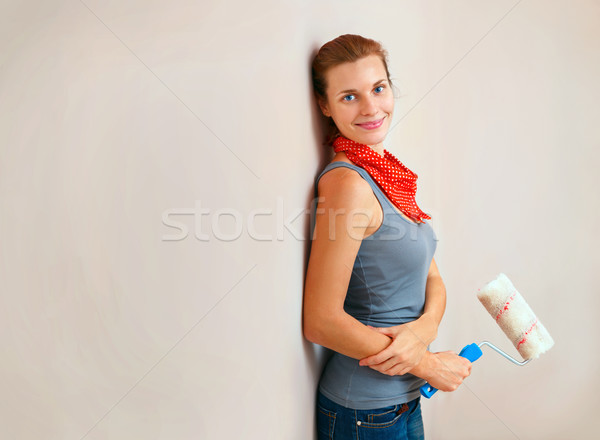 Stock photo: Happy woman with roller brush standing against wall.