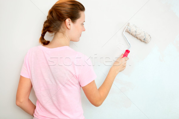 Stock photo: Young woman painting wall with roller brush.