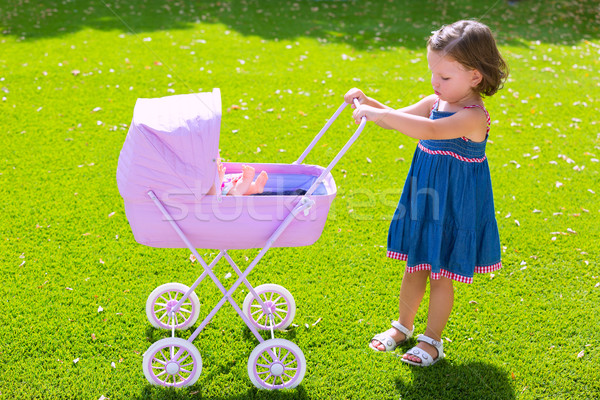 Toddler kid girl playing with baby cart in green turf Stock photo © lunamarina