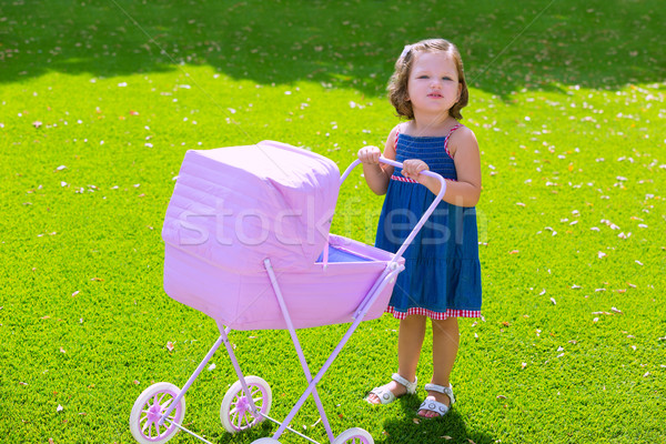Toddler kid girl playing with baby cart in green turf Stock photo © lunamarina