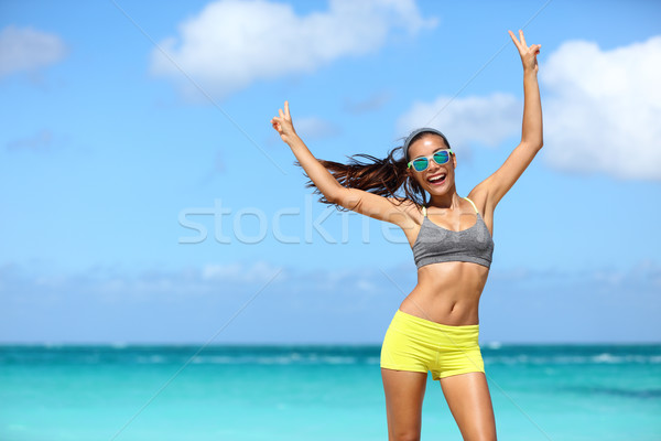 Happy cheerful fitness woman in sunglasses winning arms up doing v hand signs Stock photo © Maridav