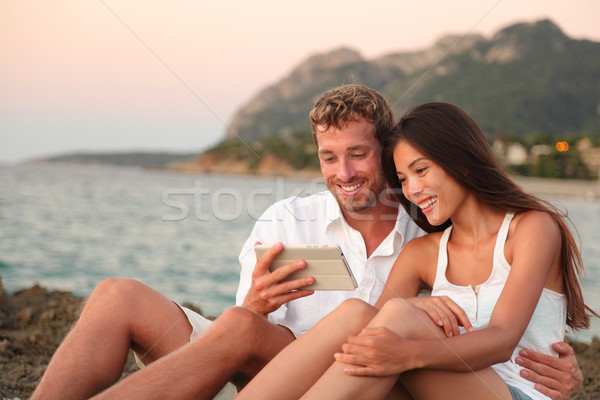 Romantic couple relaxing on beach using tablet app Stock photo © Maridav