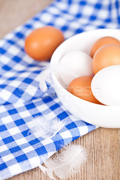 eggs in a bowl, towel and feathers on rustic wooden table Stock photo © marylooo