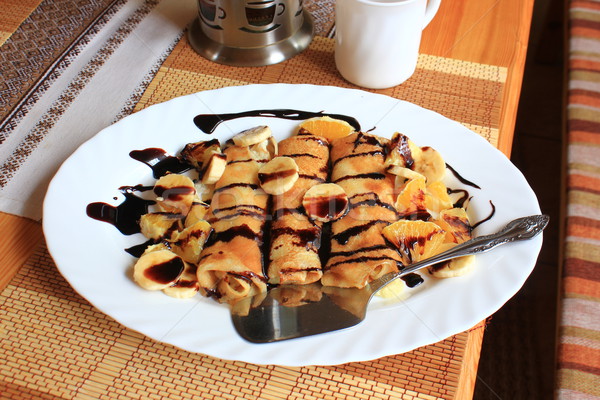 Pancakes stuffed with semolina, bananas and oranges drenched dark chocolate Stock photo © MarySan