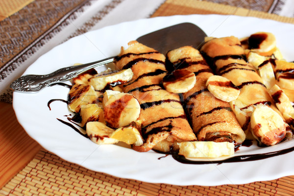 Pancakes stuffed with semolina, bananas and oranges drenched dark chocolate Stock photo © MarySan
