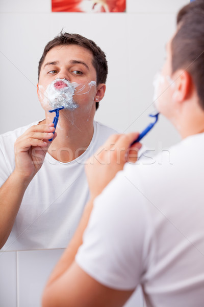 photo of handsome young man shaving and looking at himself in th Stock photo © Massonforstock