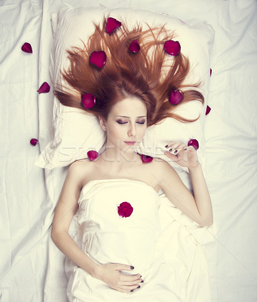 Beautiful red-haired girl in bed with rose petal. Studio shot. Stock photo © Massonforstock