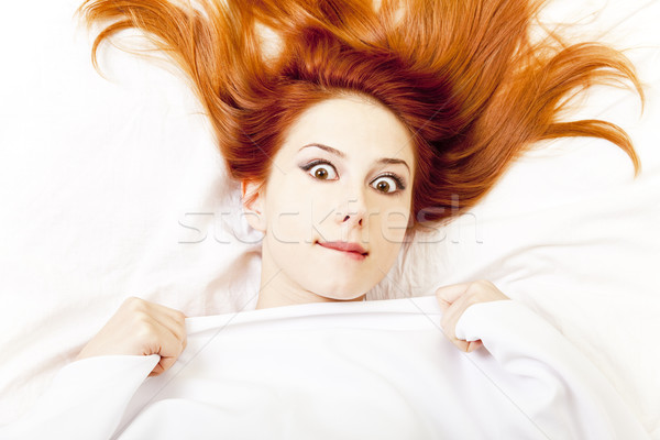 Stock photo: Surprised red-haired girl in bed. Studio shot.