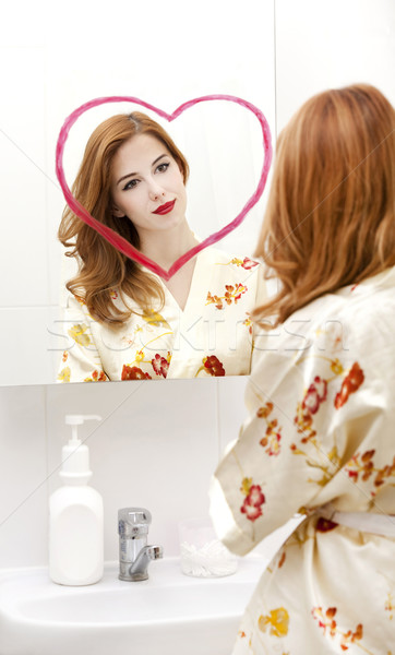 Redhead girl near mirror with heart it in bathroom. Stock photo © Massonforstock