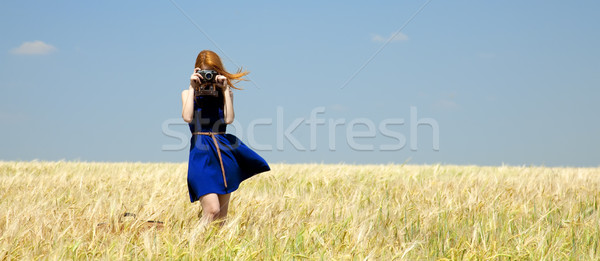 Stock photo: Redhead girl at spring wheat field with retro camera.