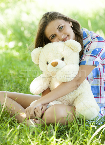 Stock photo: Beautiful teen girl with Teddy bear in the park at green grass.