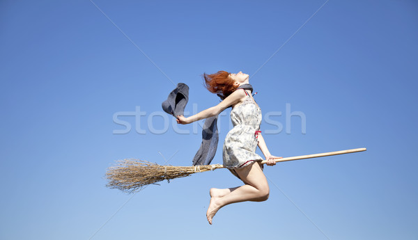 Stock photo: Young red-haired witch on broom flying in the sky