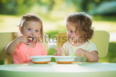 Stock photo: Two little girls sitting at a table and eating together against green lawn