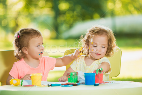 Stock photo: Two-year old girls painting with poster paintings together against green lawn