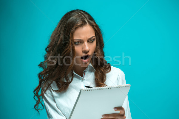 Surprised young business woman with pen and tablet for notes on blue background Stock photo © master1305