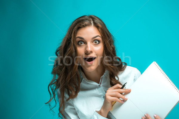 Surprised young business woman with pen and tablet for notes on blue background Stock photo © master1305